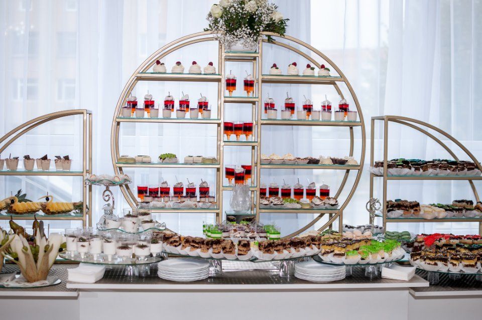 Buffet di dolci: scaffali dorati decorati espongono pasticcini, bevande a strati e altri dolci su uno sfondo bianco.