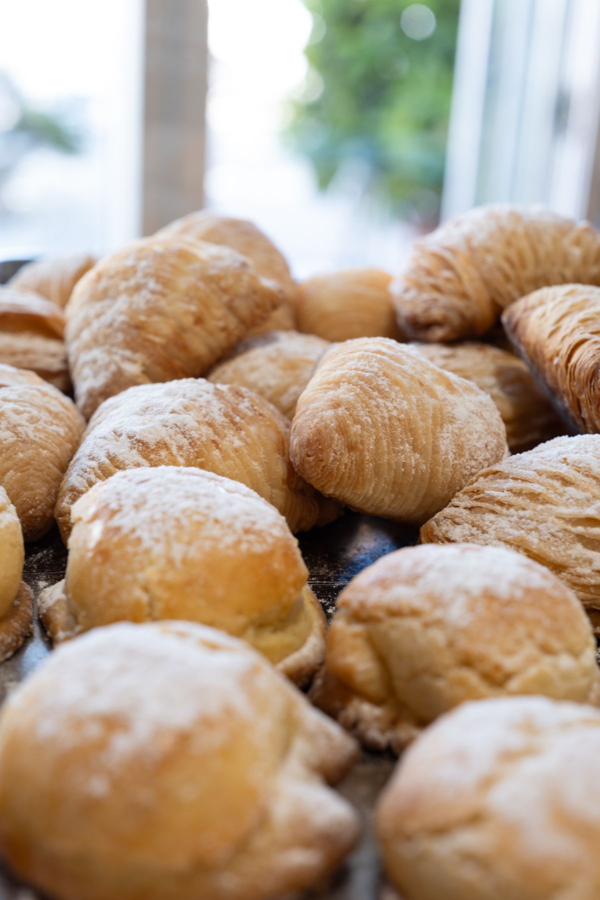 Primo piano di un vassoio pieno di pasticcini dorati spolverati di zucchero a velo.