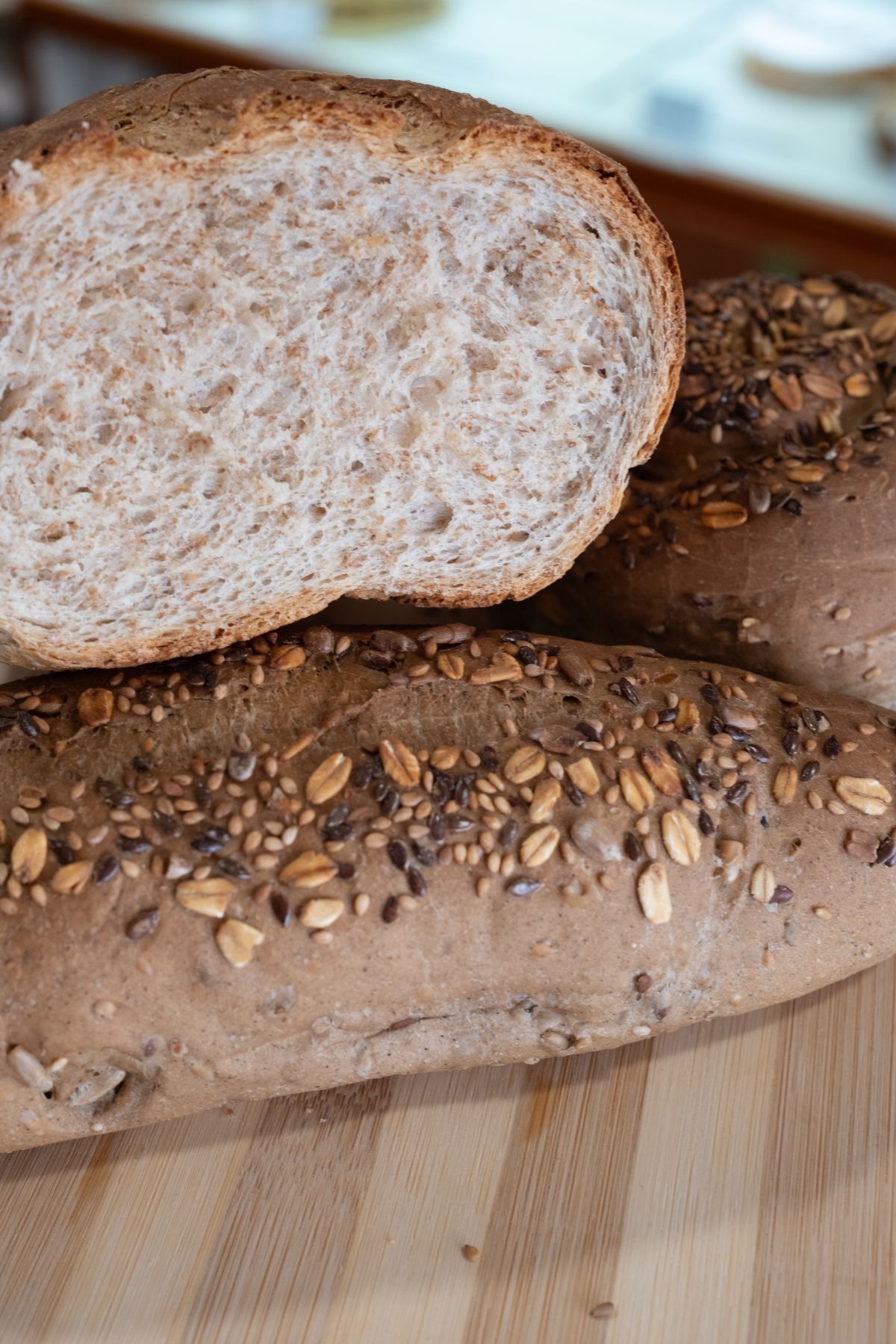 Primo piano di tre pagnotte di pane integrale su una superficie di legno, una tagliata per mostrare l'interno.