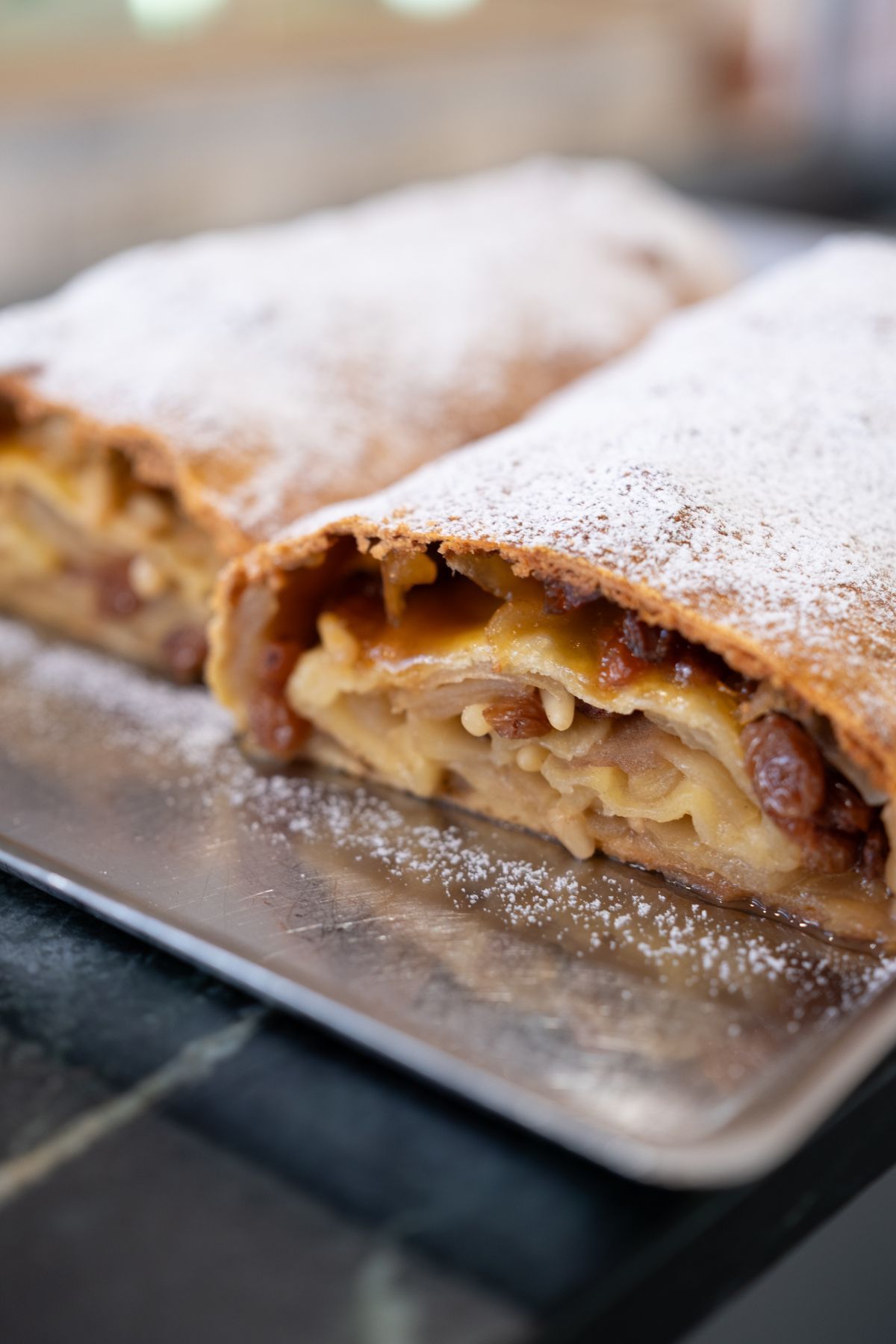Strudel di mele spolverato con zucchero a velo su un vassoio di metallo.