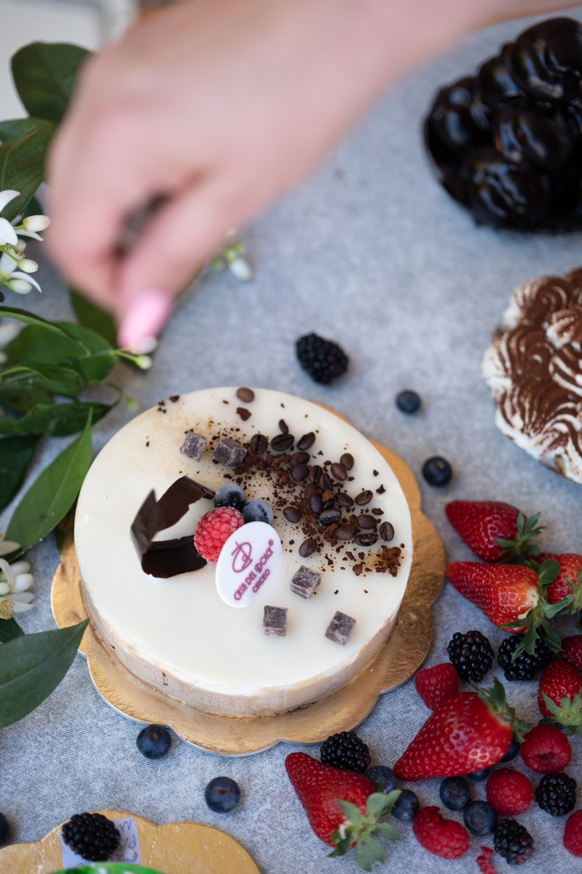 Cheesecake con frutti di bosco, cioccolato e qualcuno che mette dei fiori lì vicino.
