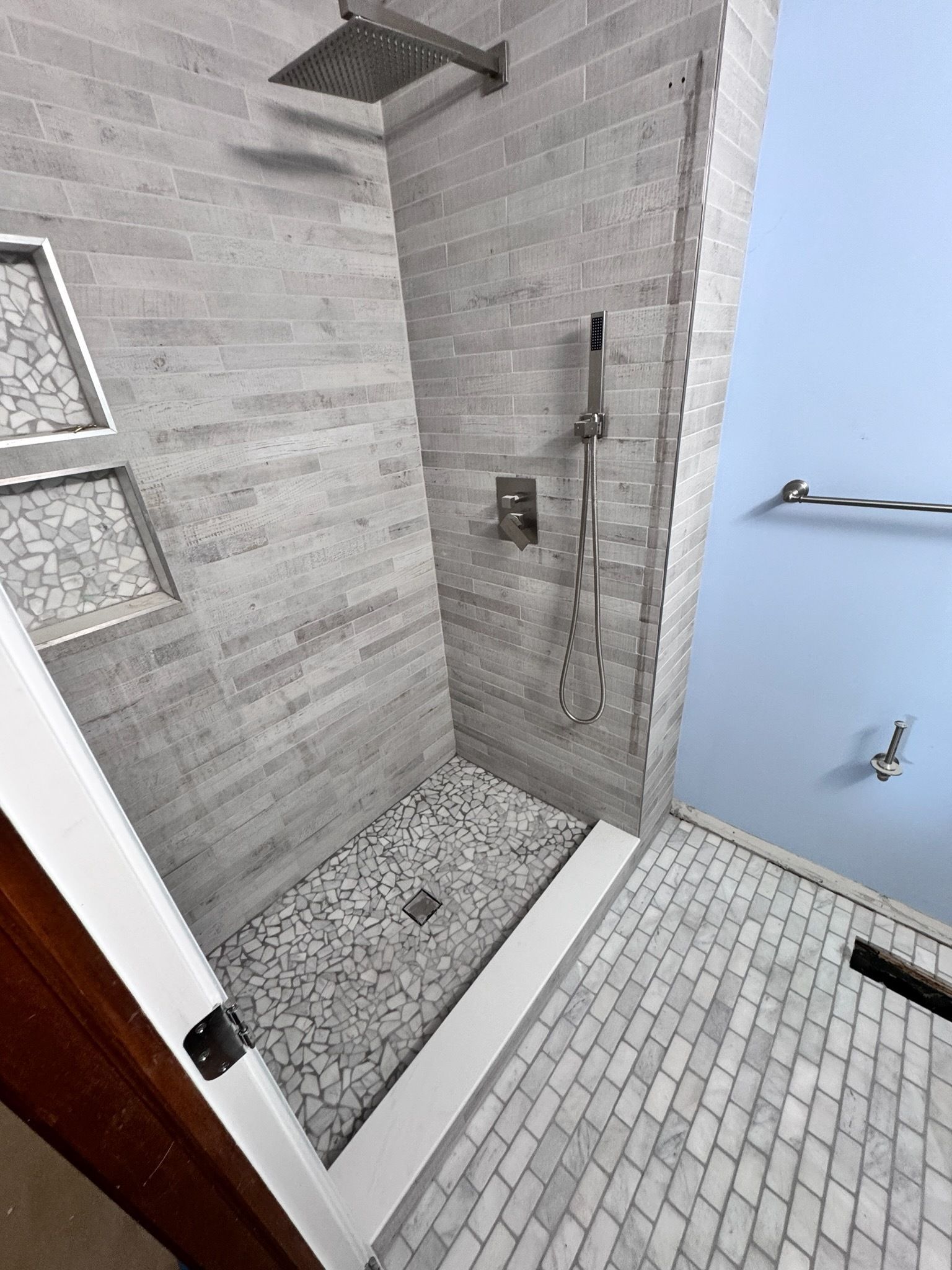 Tiled walk-in shower with handheld showerhead, bench, and a small adjacent tiled floor area