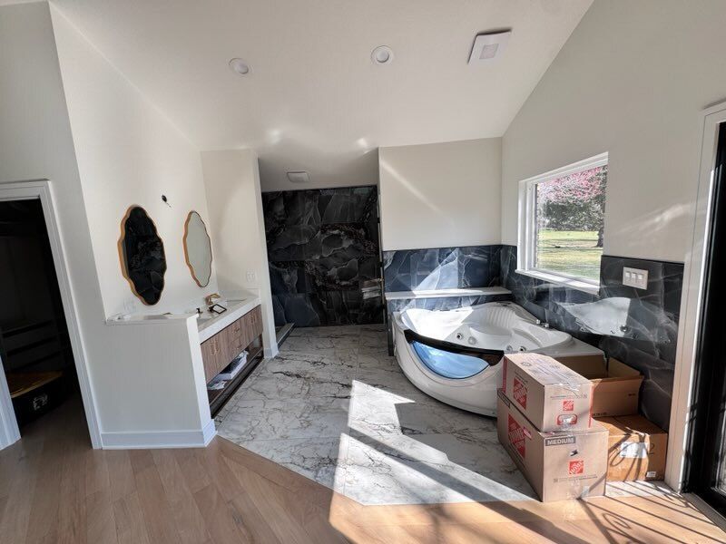 Unfinished bathroom with black vanity, dark stone shower, and construction boxes on the floor