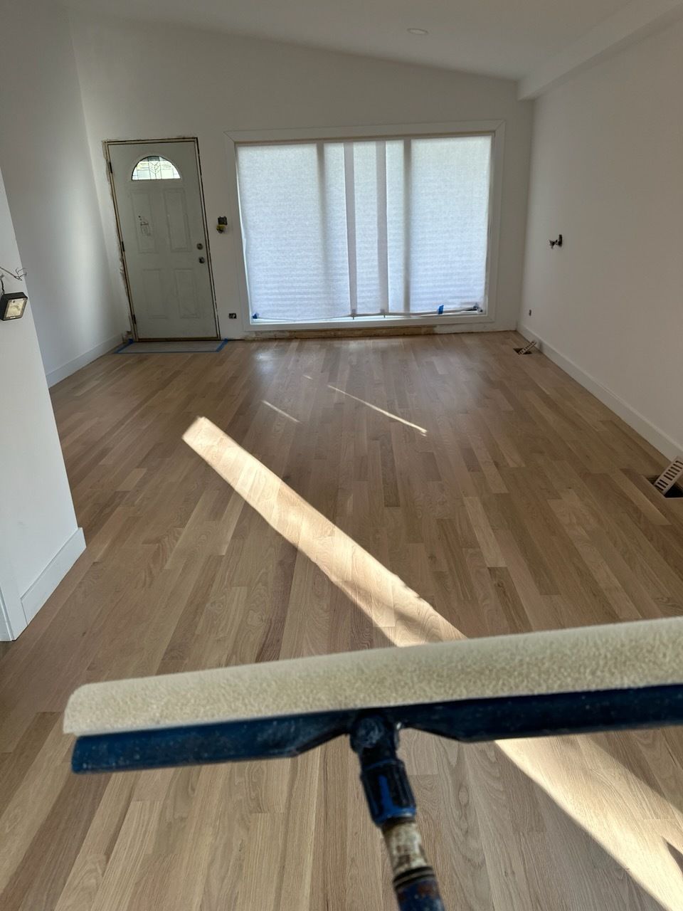 Empty room with wood floors, large window, and a mop in the foreground.