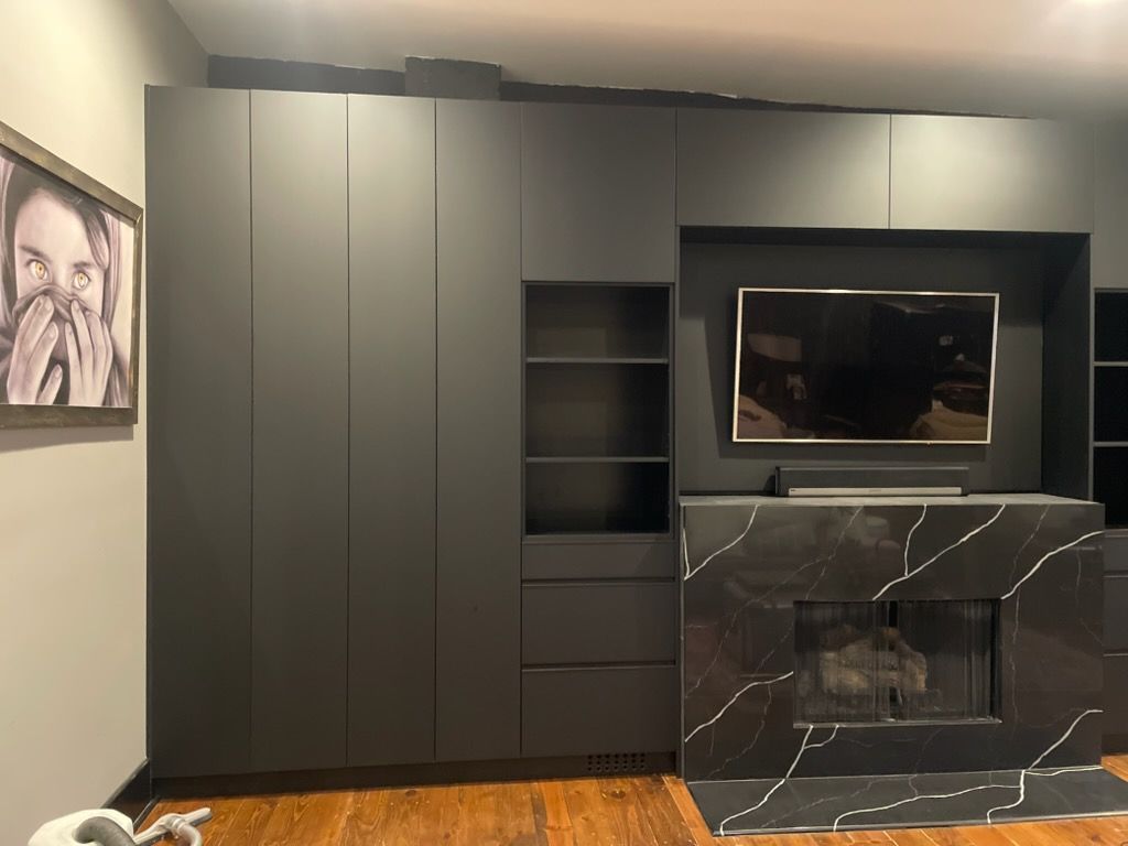 Modern living room wall with dark built-in cabinets, TV, black marble fireplace, and framed art on the left.