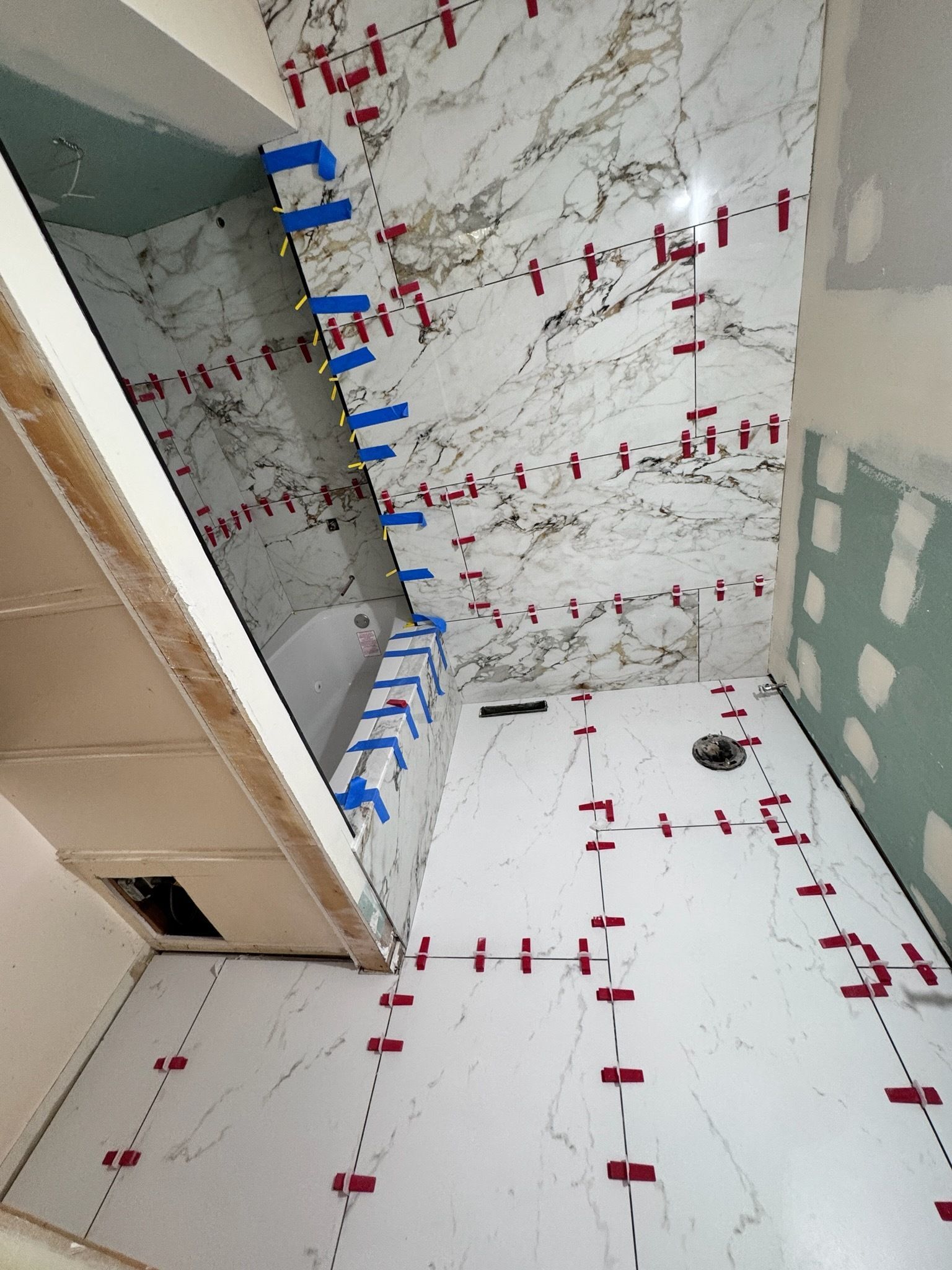 Partially tiled bathroom under construction with drywall, blue spacers, and red markings on walls and floor