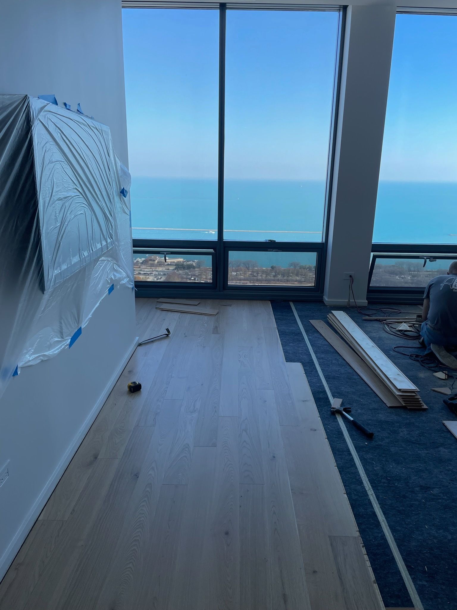 Partially renovated room with ocean view through large windows, white walls, and materials on the floor