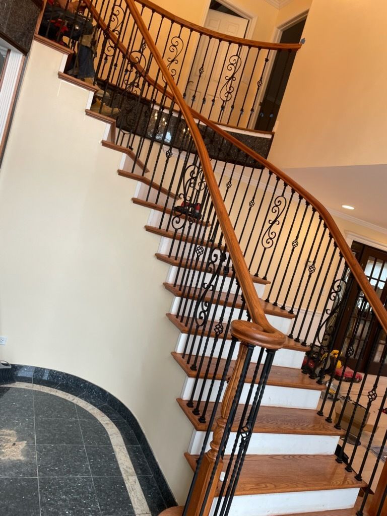 Indoor curved staircase with wooden steps, black iron railing, and a tiled floor below.
