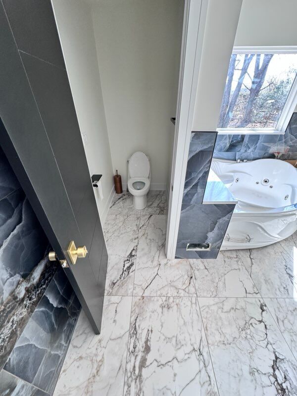 Small bathroom with white toilet, marble-pattern tile floor, and partially open dark shower door.