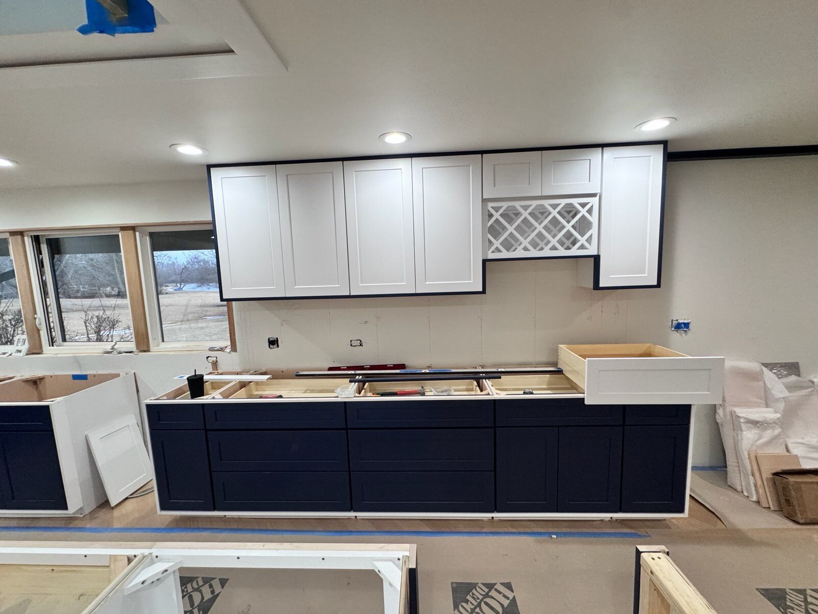 Kitchen remodel in progress with white upper cabinets, navy island, and countertop tools.