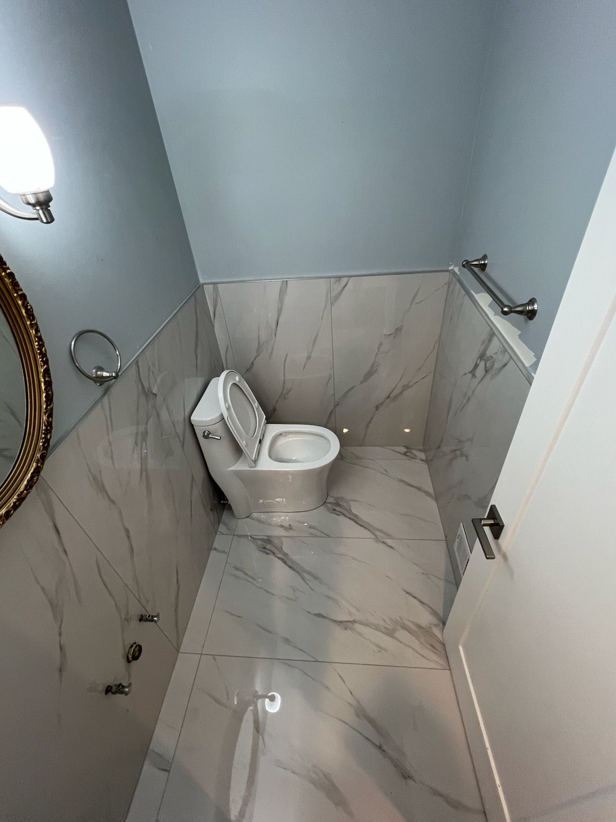Small bathroom with a white toilet and marble-patterned walls and floor, viewed from the doorway