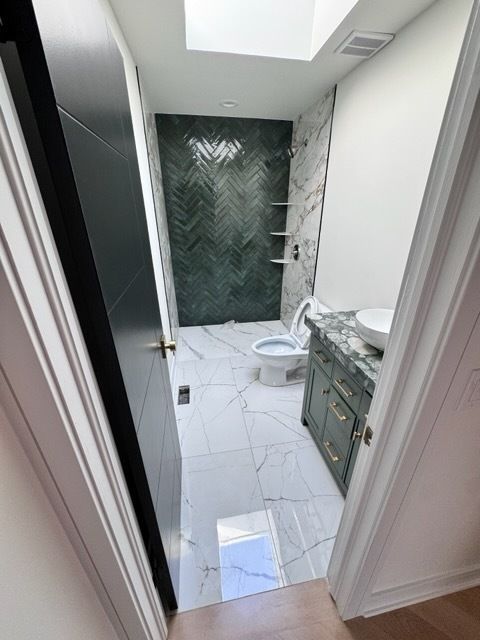 Narrow bathroom with white tile, green marble shower wall, toilet, and vanity sink.