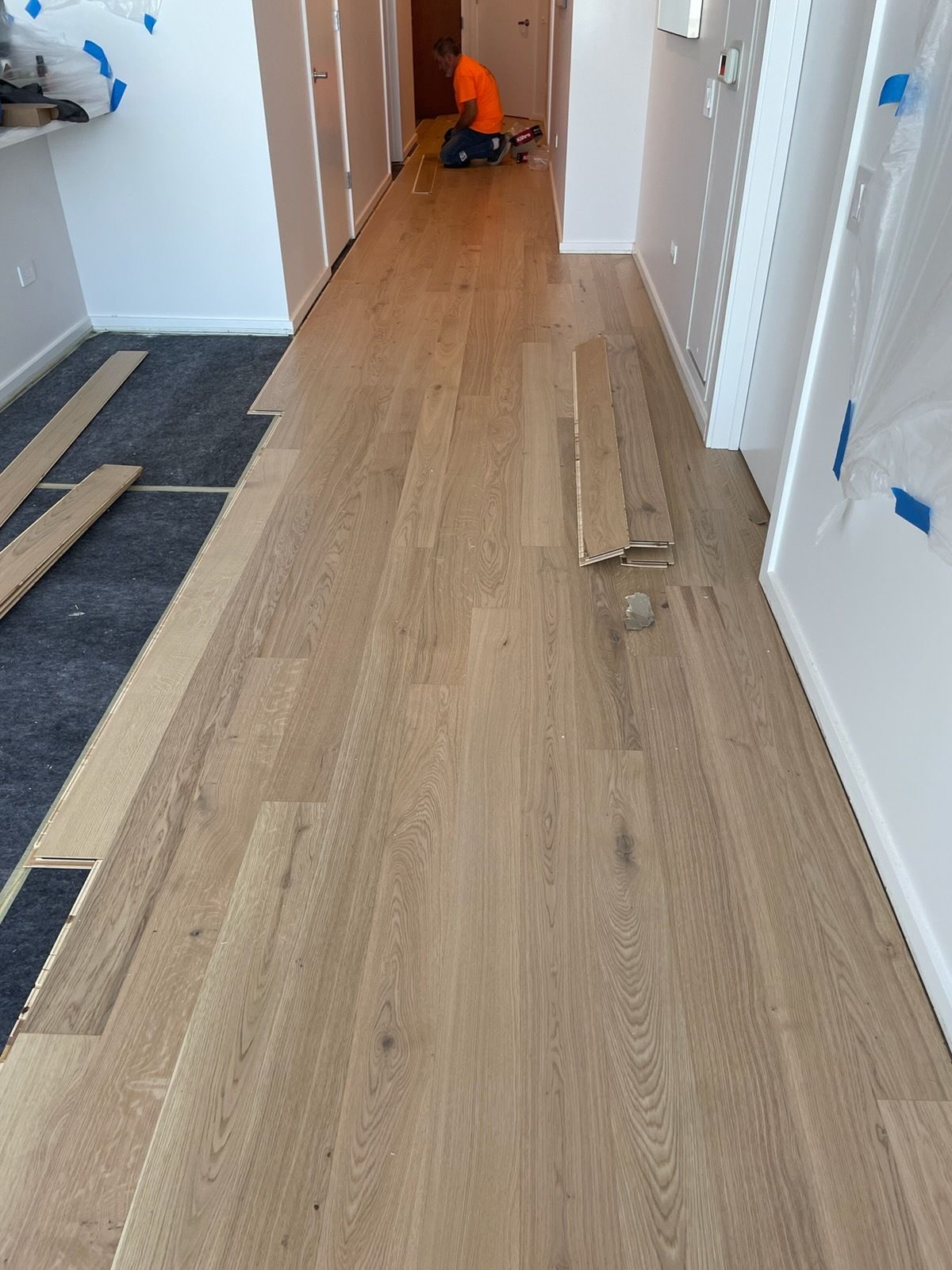 Partially installed light wood flooring in a hallway with tools and loose planks on the floor