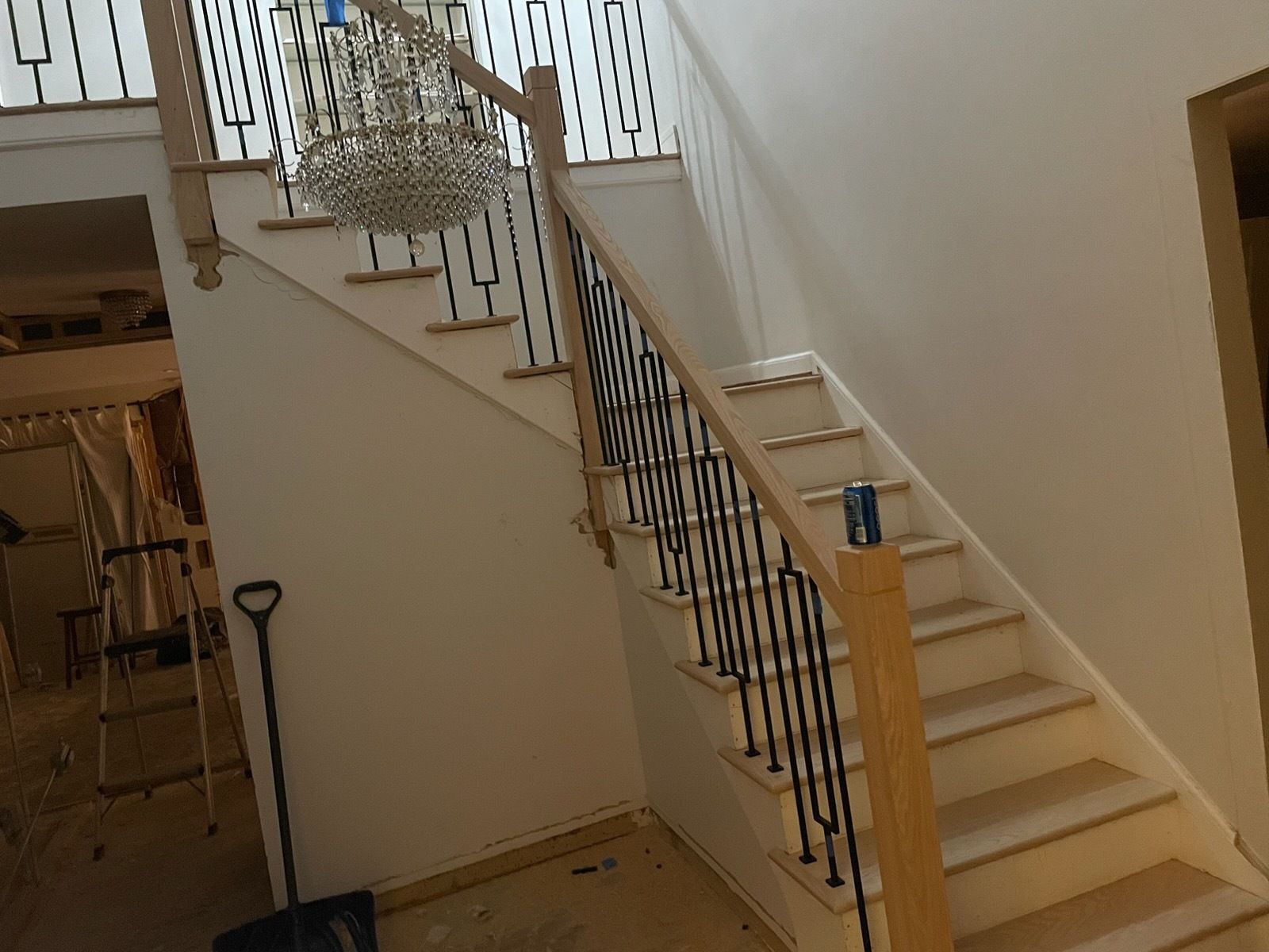 Staircase with white walls, wooden steps, and black wrought-iron railing in a hallway