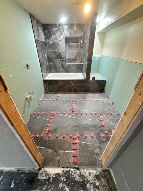 Bathroom under construction with tiled shower, gray flooring, and red spacer markers on the floor.