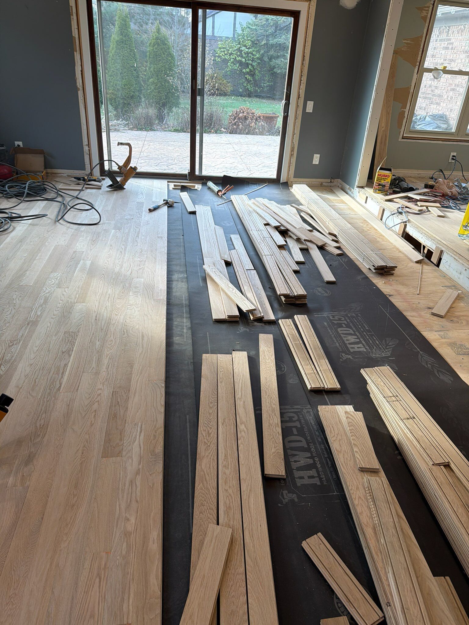 Partially installed hardwood flooring in a room with sliding glass doors and daylight coming in