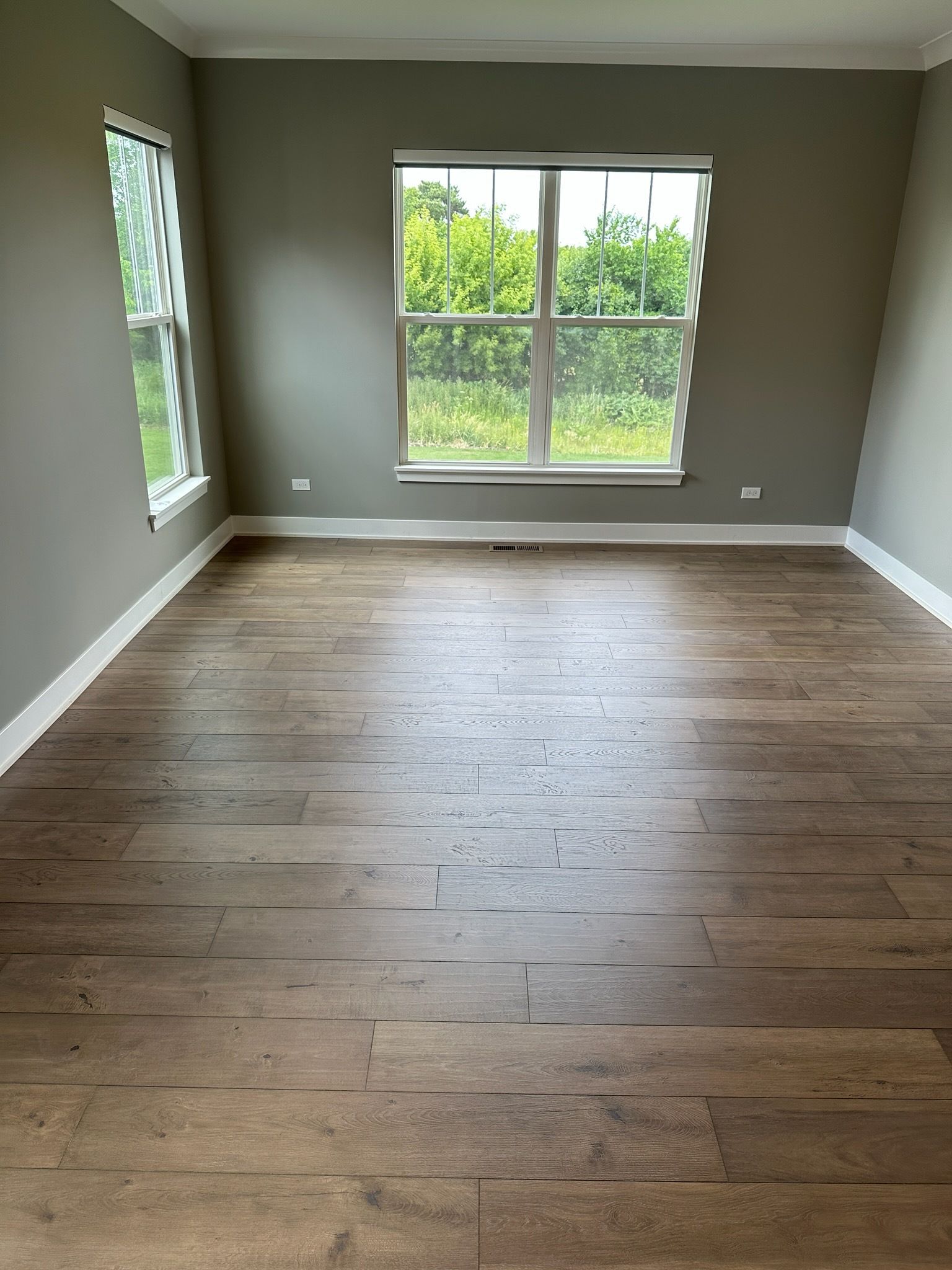 Empty room with wood floors, gray walls, and large windows overlooking greenery.