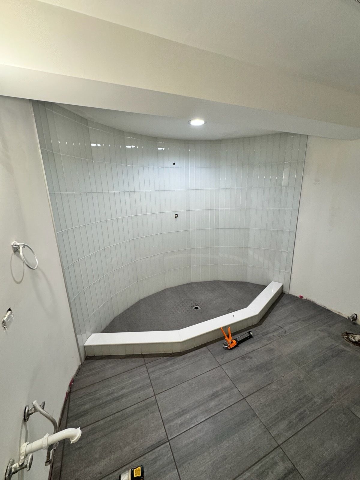 Empty tiled shower stall with gray floor, white walls, and a built-in bench.