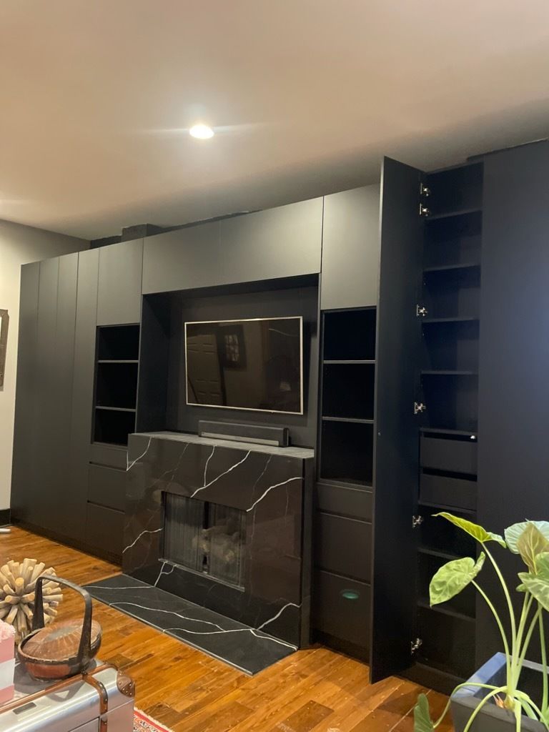 Black built-in media wall with TV, shelves, and marble fireplace in a modern living room