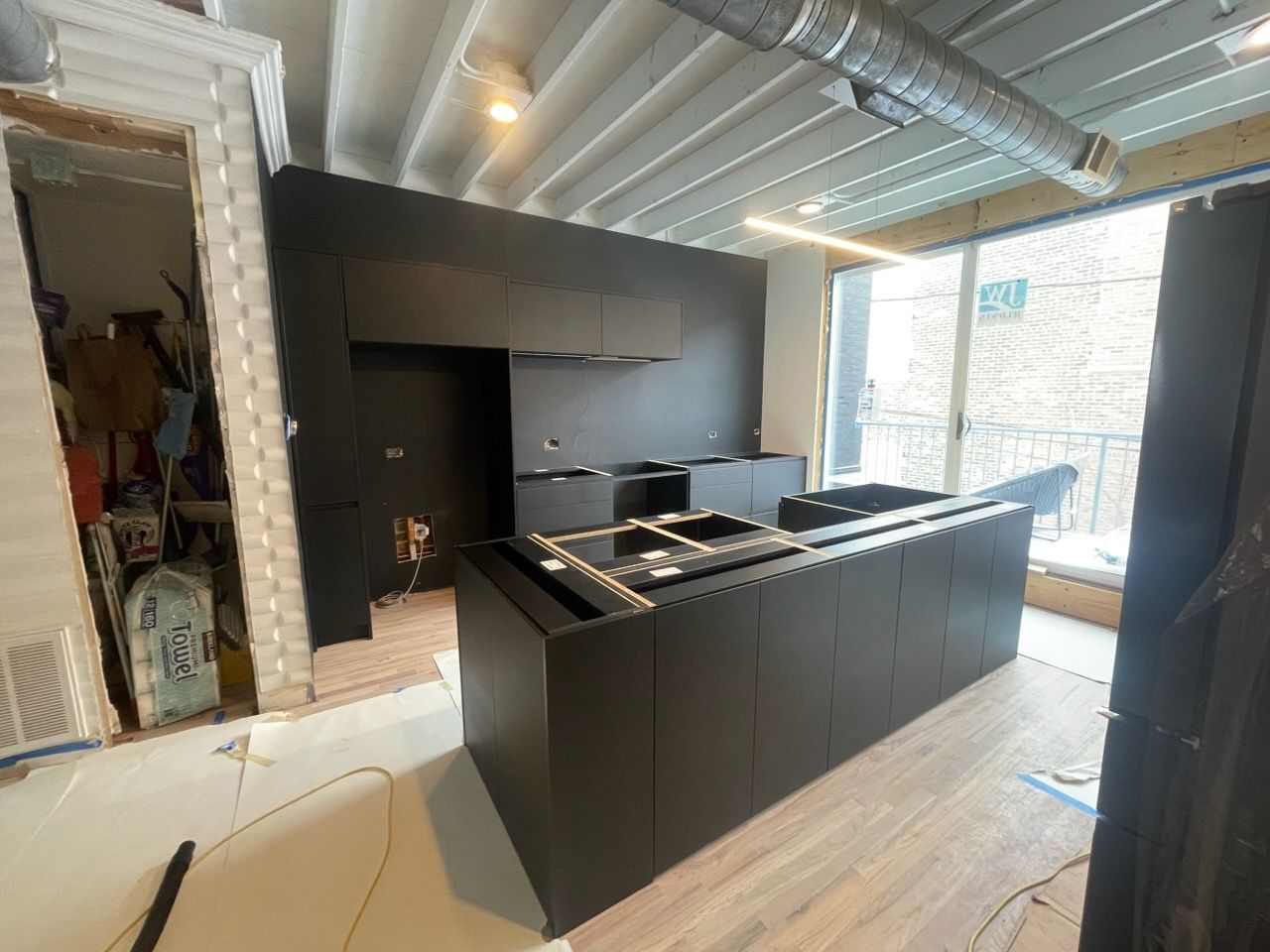 Modern kitchen showroom with dark cabinets, island, and bright windows under construction ceilings