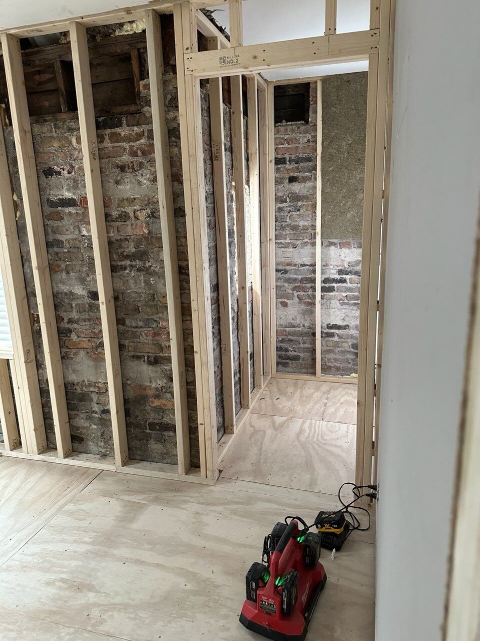 Exposed wall framing in a renovation room with a red tool on the floor and bare subfloor.
