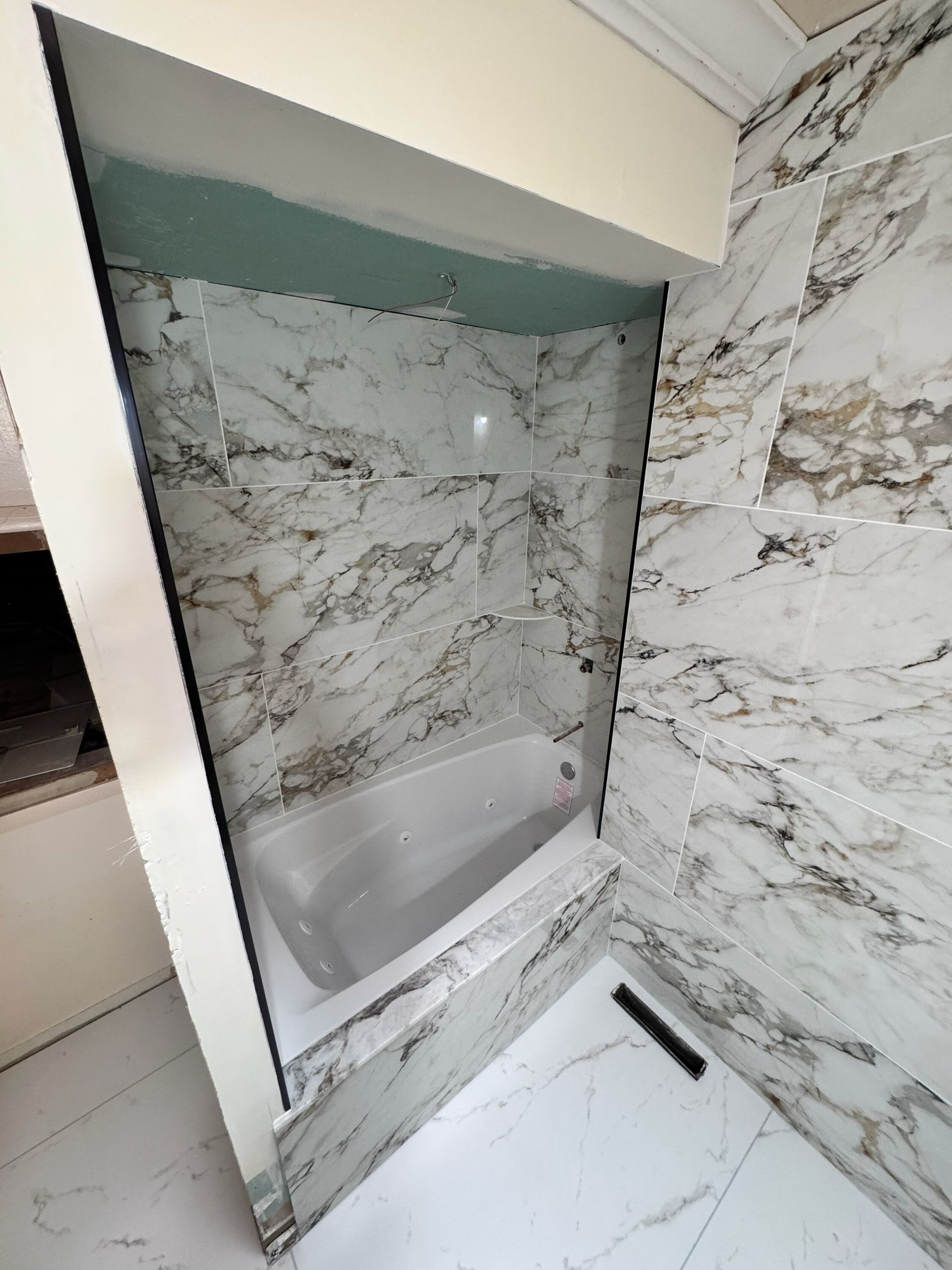 Marble-tiled shower nook with a built-in shelf and handheld showerhead in a modern bathroom