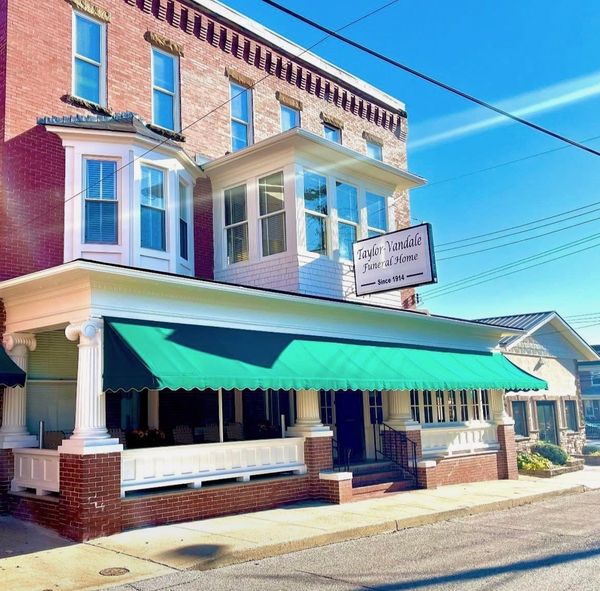 Historic brick storefront with green awning and white porch under a bright blue sky