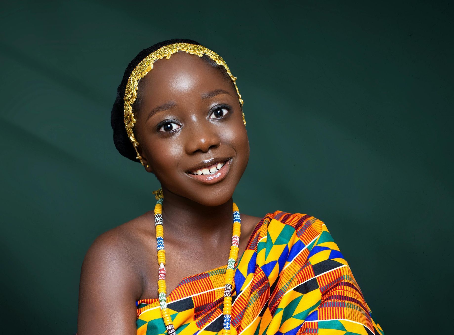 A young woman in a traditional Ashanti kente cloth is smiling for the camera.