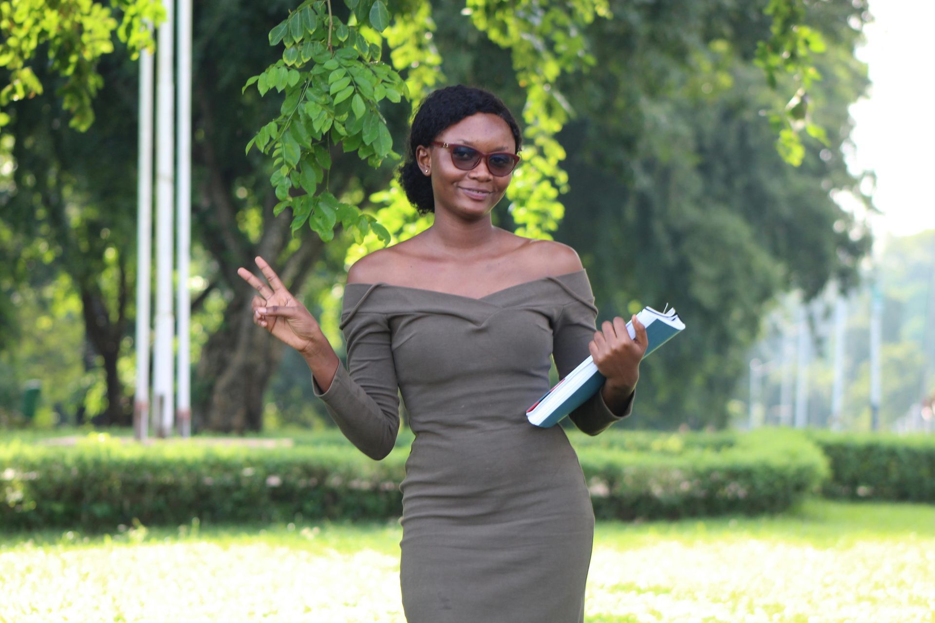 A woman in a green dress is holding a book and giving a peace sign.