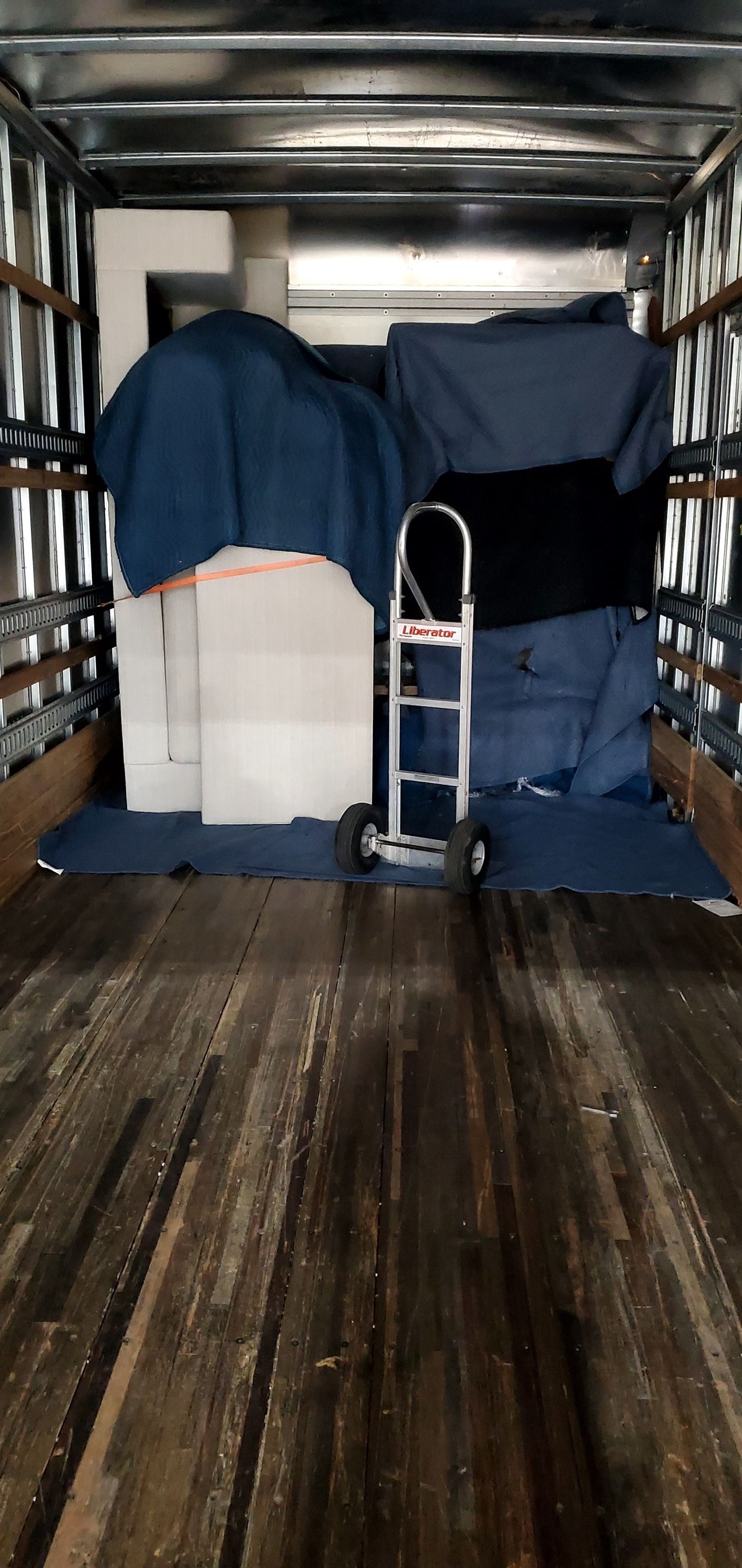 The inside of a moving truck filled with furniture and a dolly.