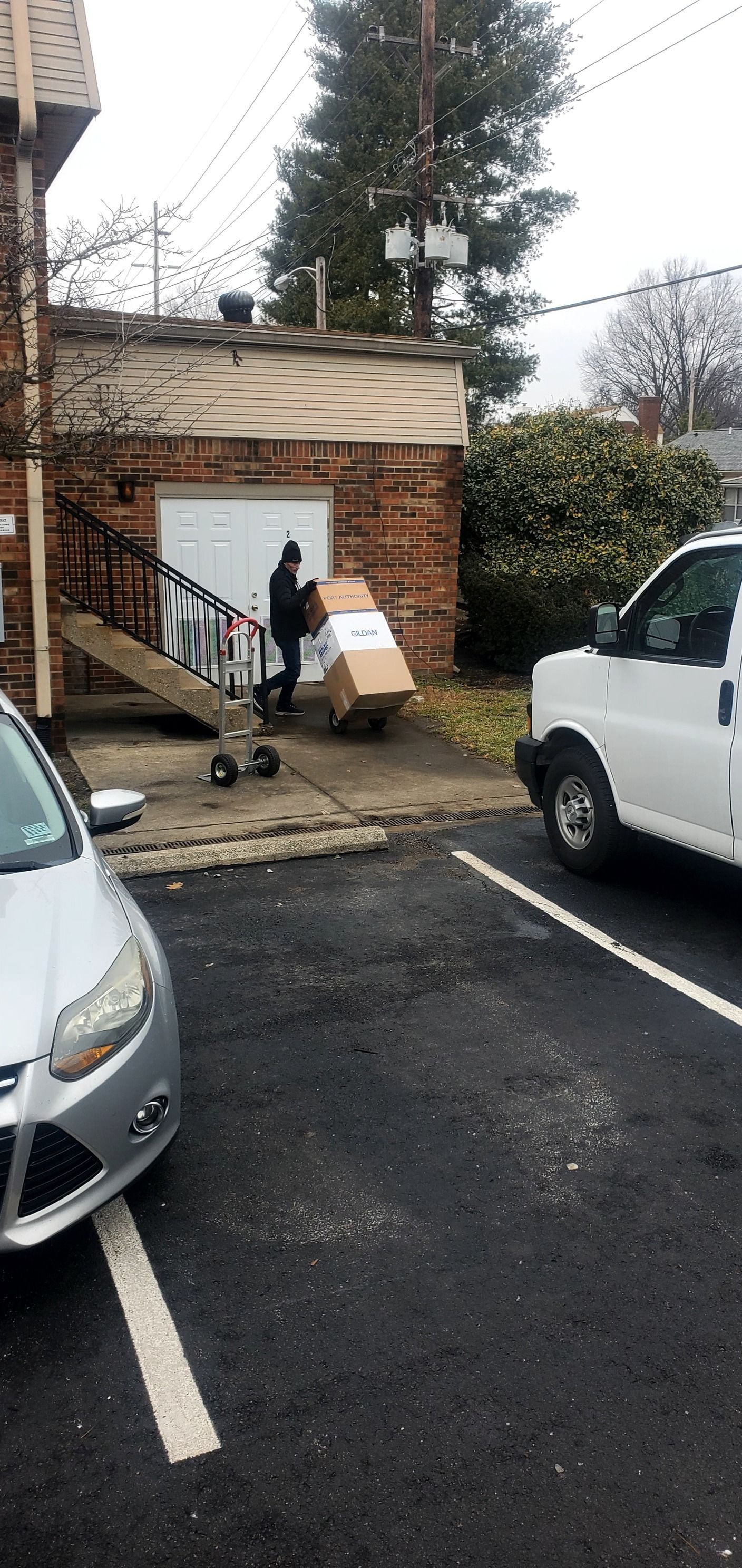A man is pushing a box on a cart in a parking lot.