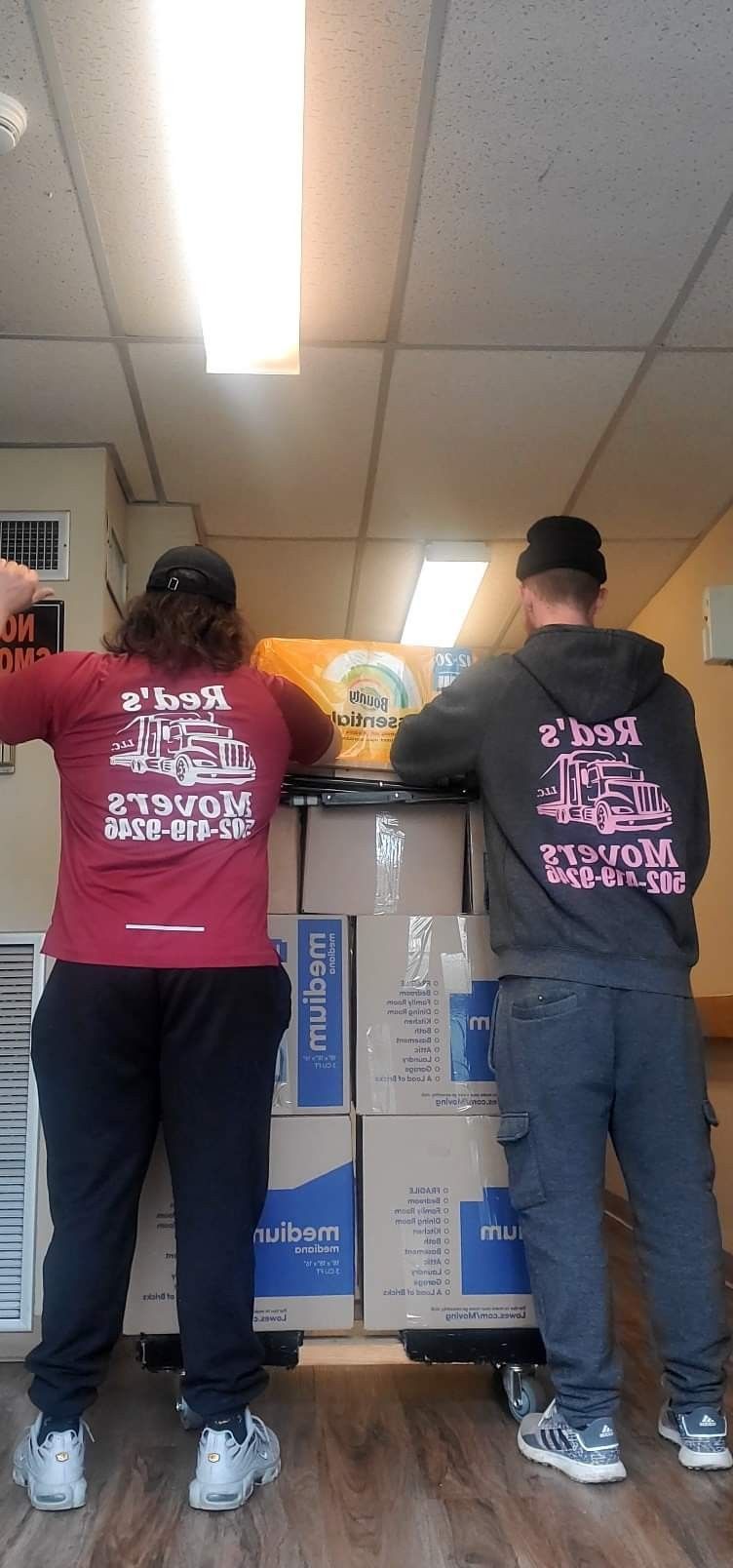 A man and a woman are standing next to each other in front of a cart filled with boxes.