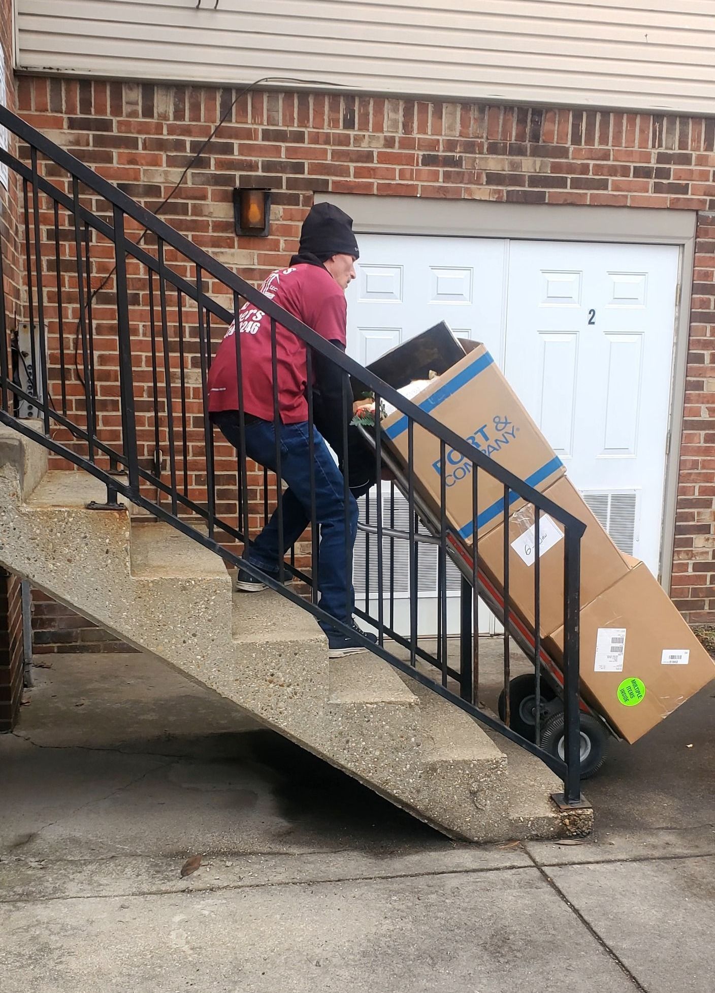 A man is pushing a cardboard box up a set of stairs.