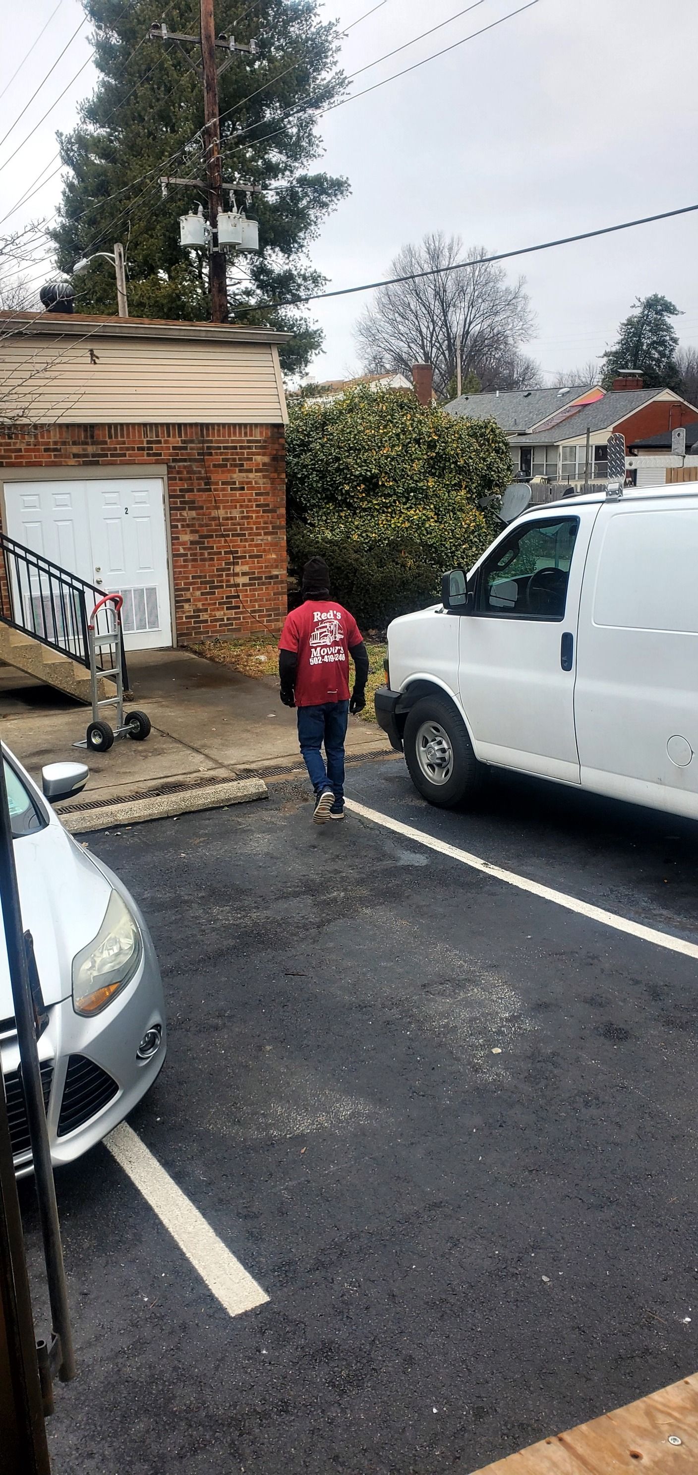 A man in a red shirt is walking towards a white van in a parking lot.