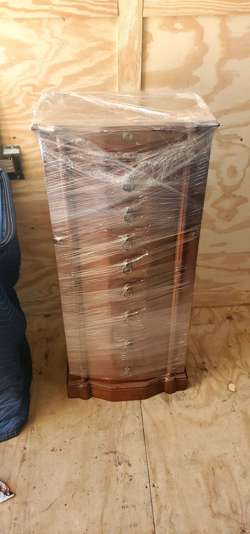 A wooden dresser wrapped in plastic is sitting on a wooden floor.