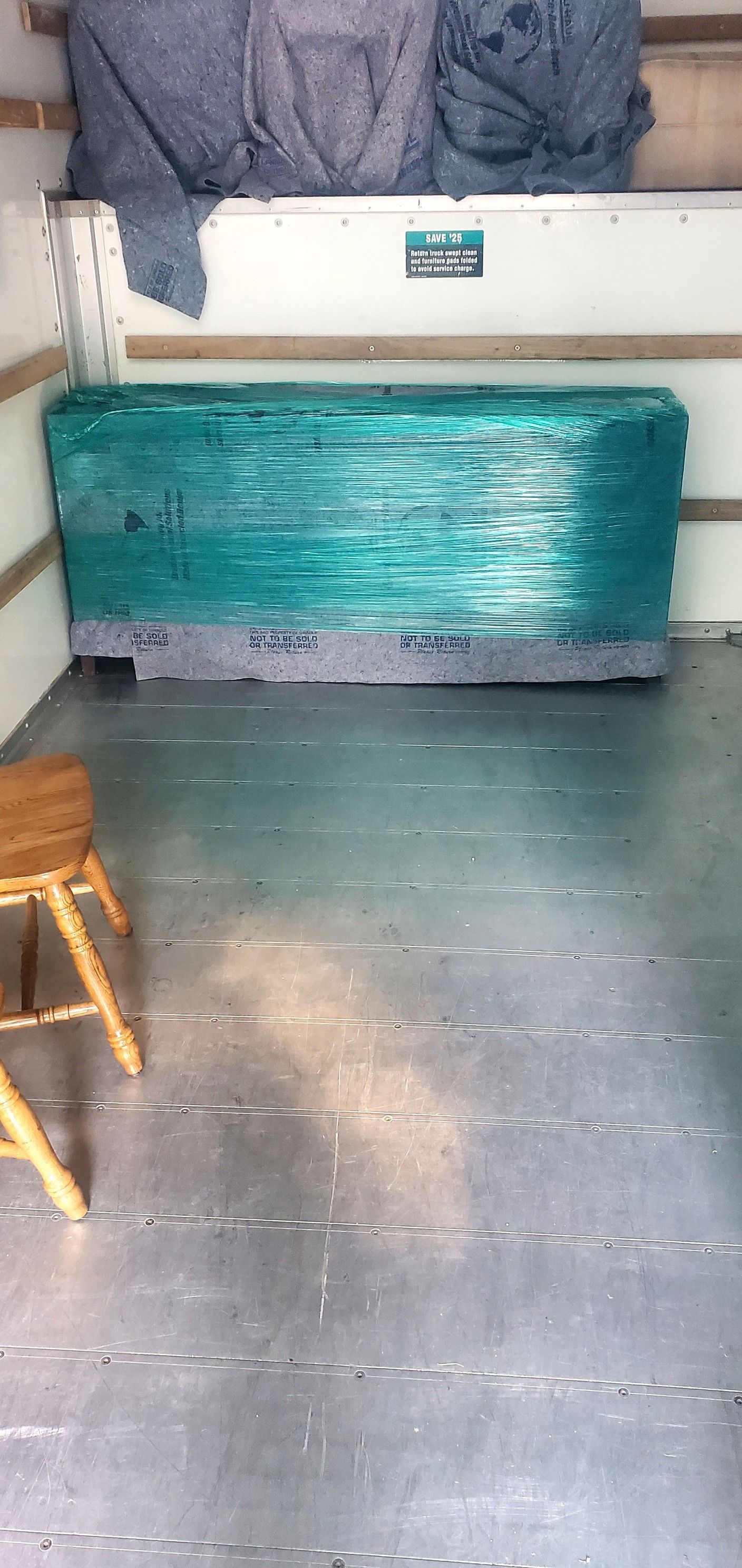 A room with a wooden stool and a box wrapped in plastic.