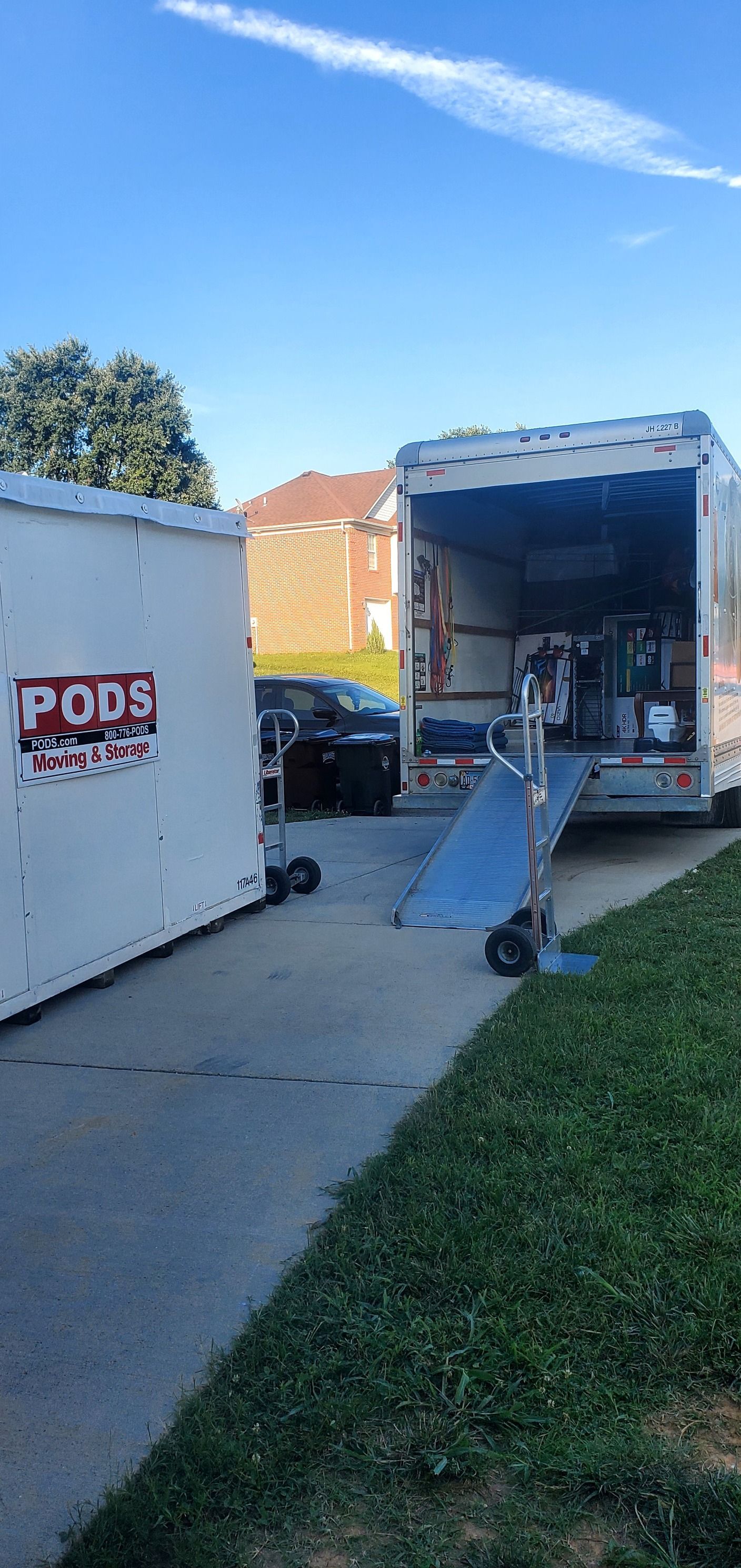 A moving truck is parked in a driveway next to a container.