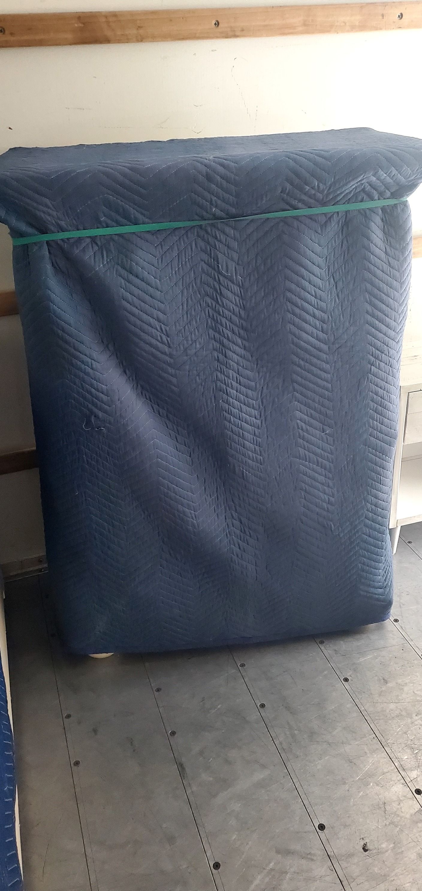A mattress is wrapped in a blue blanket in a moving truck.