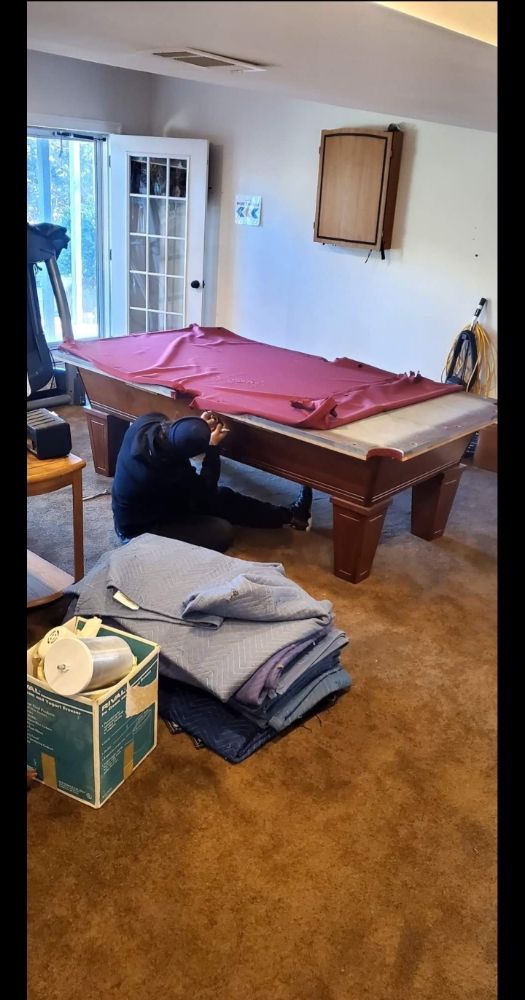 A man is kneeling under a pool table in a living room.