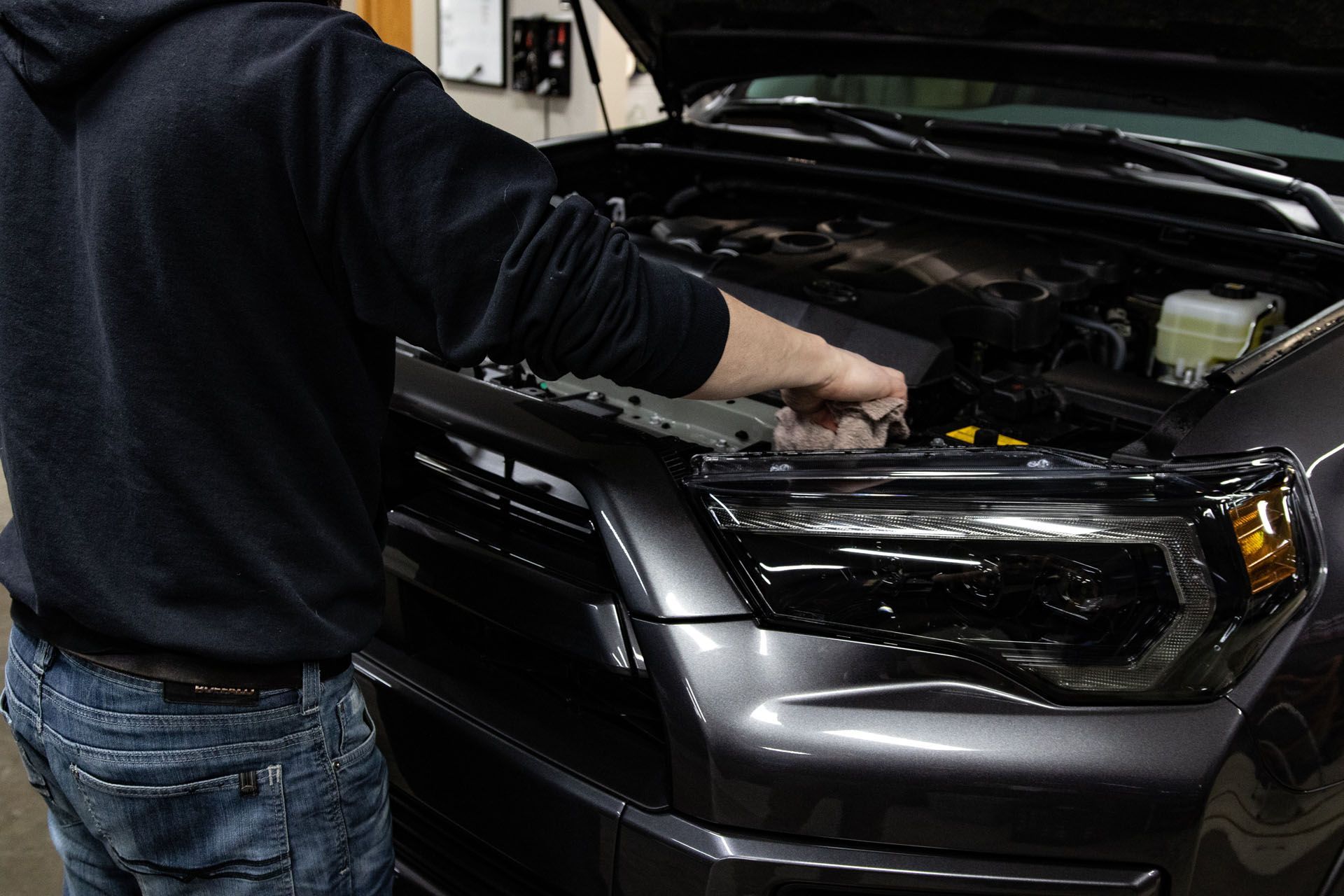 Person working under the hood of a black pickup truck in a garage