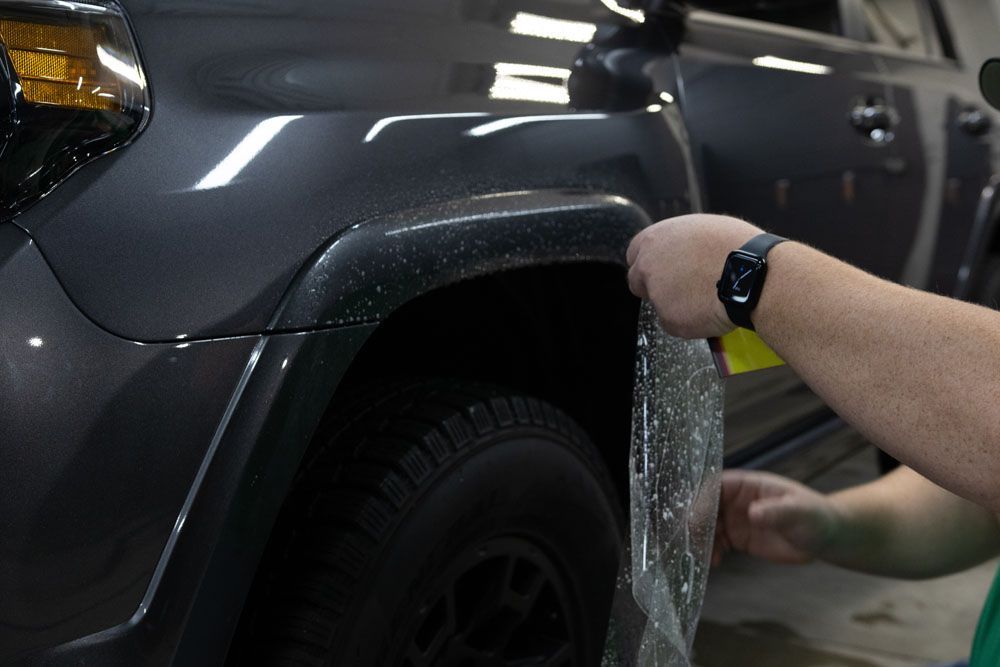 Person polishing a black car’s surface with a buffer and gloved hands