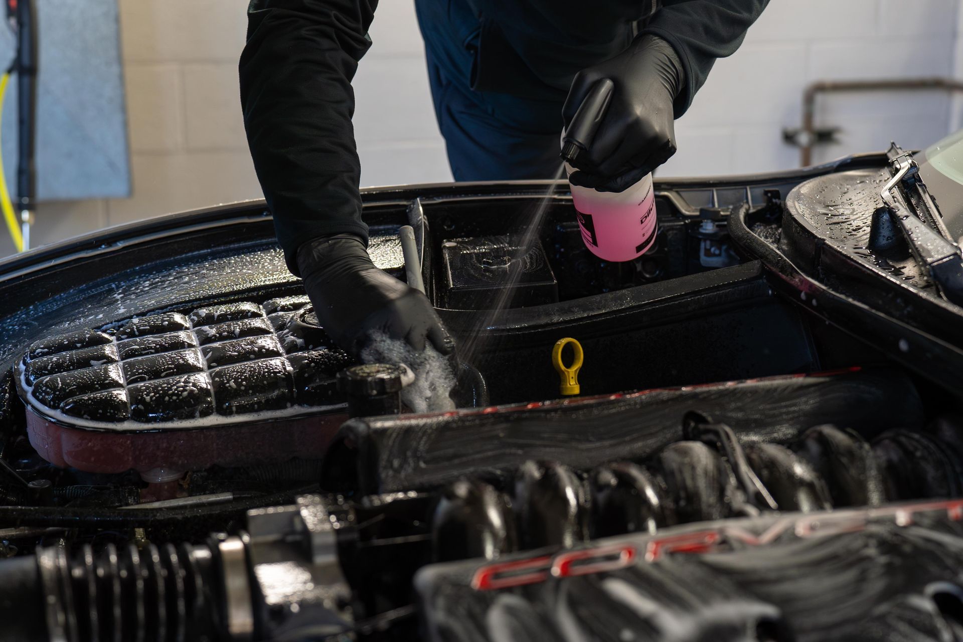 Gloved hand wiping a car engine with a red cloth