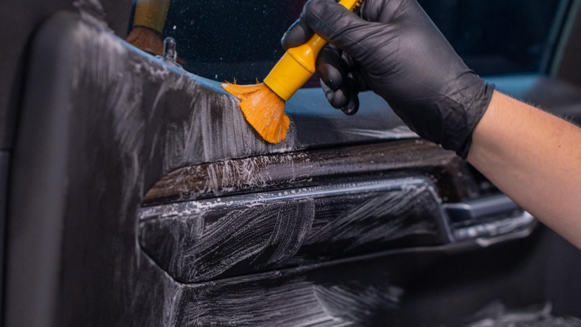 Gloved hand applying orange tool to car door, spreading soap or film during auto detailing