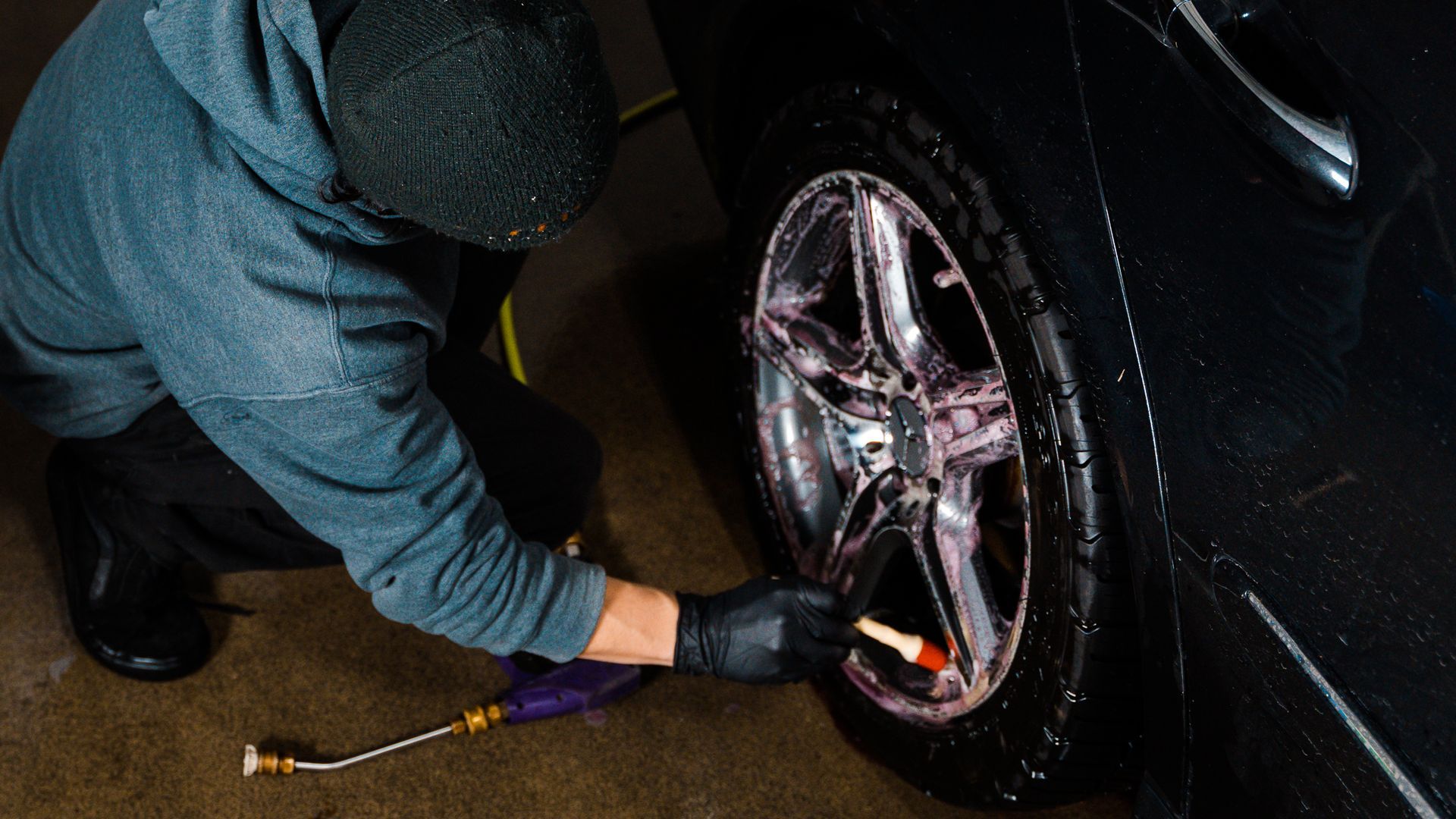 Hand wiping a dark car with a yellow cloth, polishing the rear panel near the taillight.