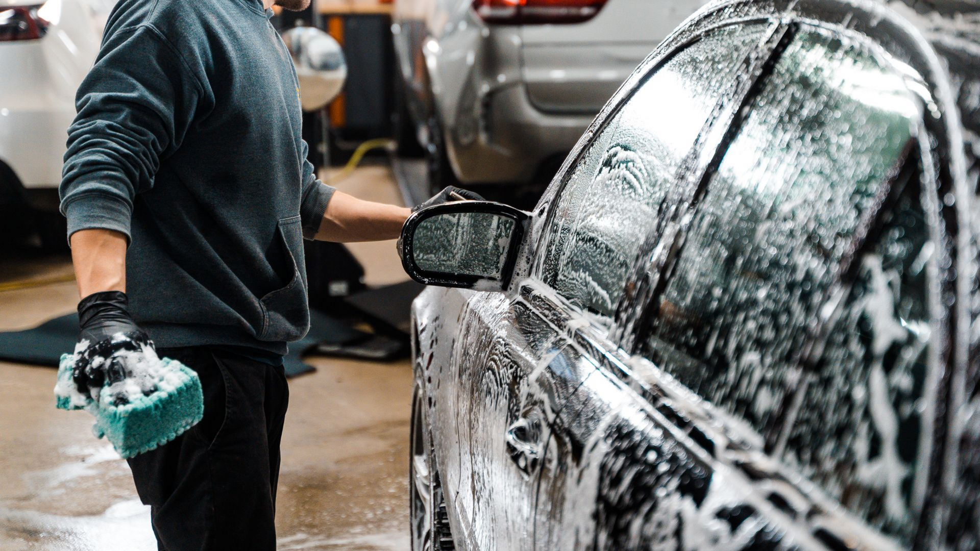 Man washing a black car with soap in an indoor car wash area