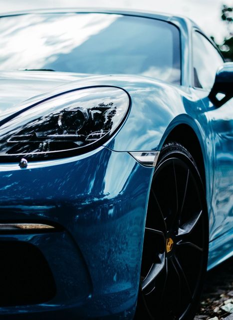 Blue sports car parked outdoors, close-up of front headlight and wheel