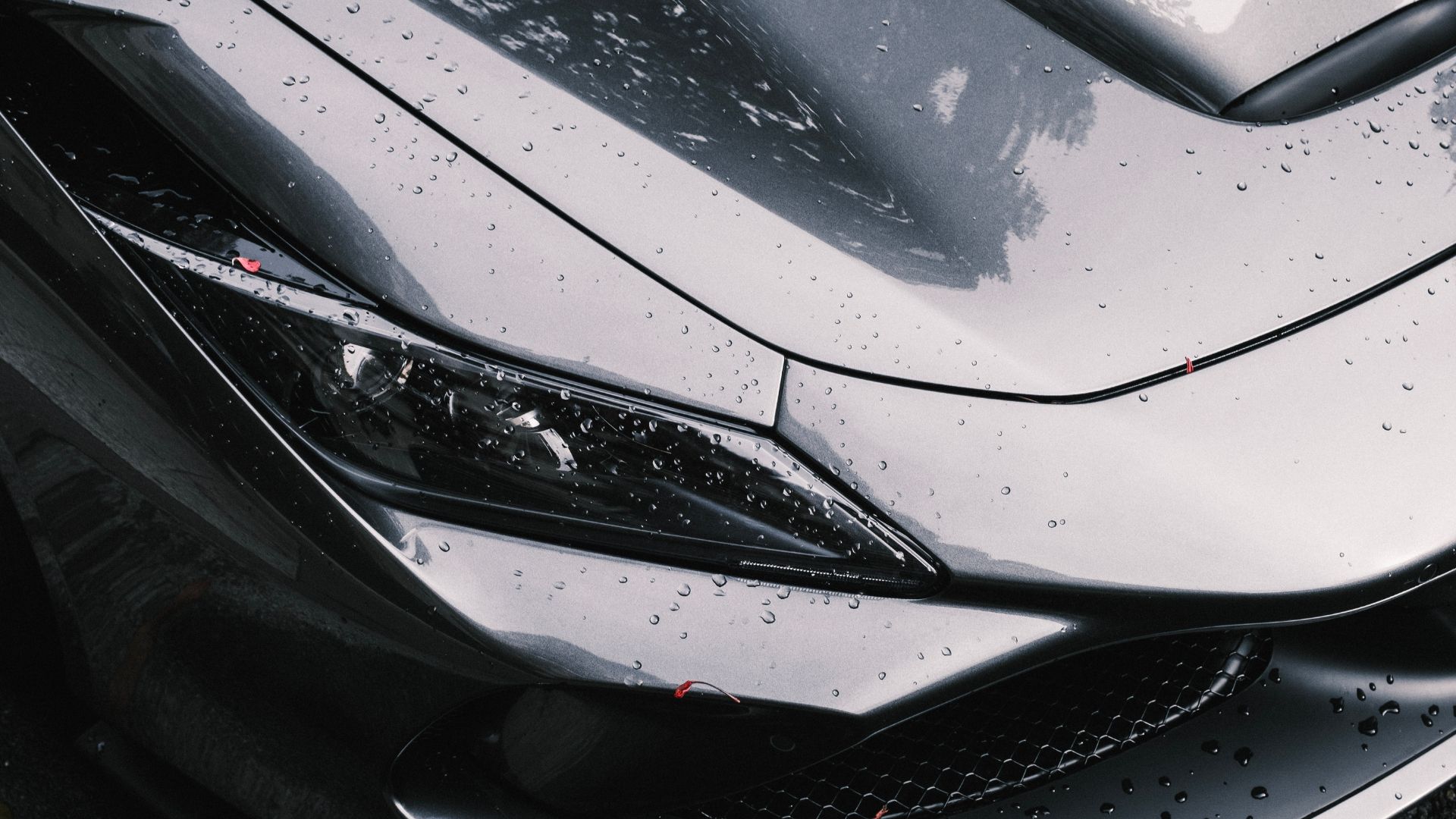 Close-up of a sleek black sports car hood and headlight with raindrops
