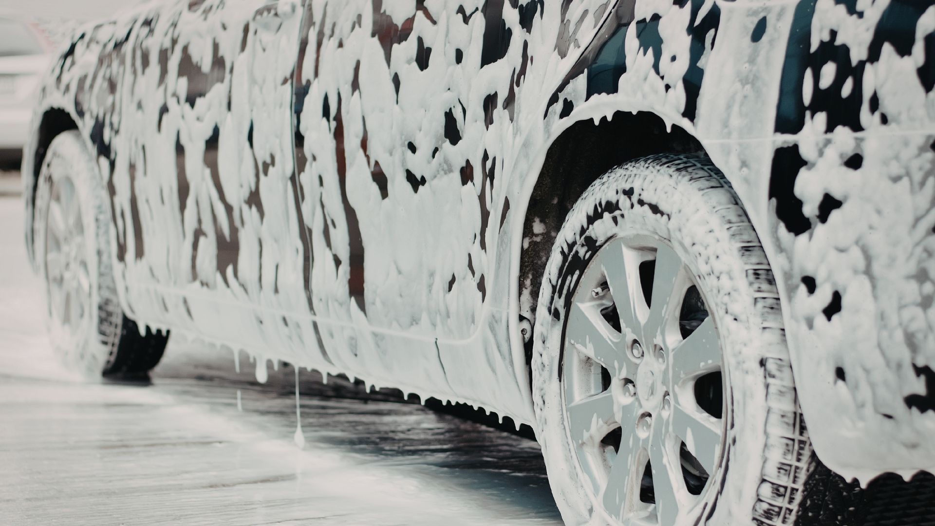 Car covered in thick white foam during a car wash, with wheels and body partially visible