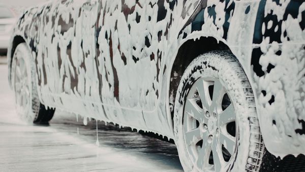 Car covered in thick white foam during a car wash, with wheels and body partially visible