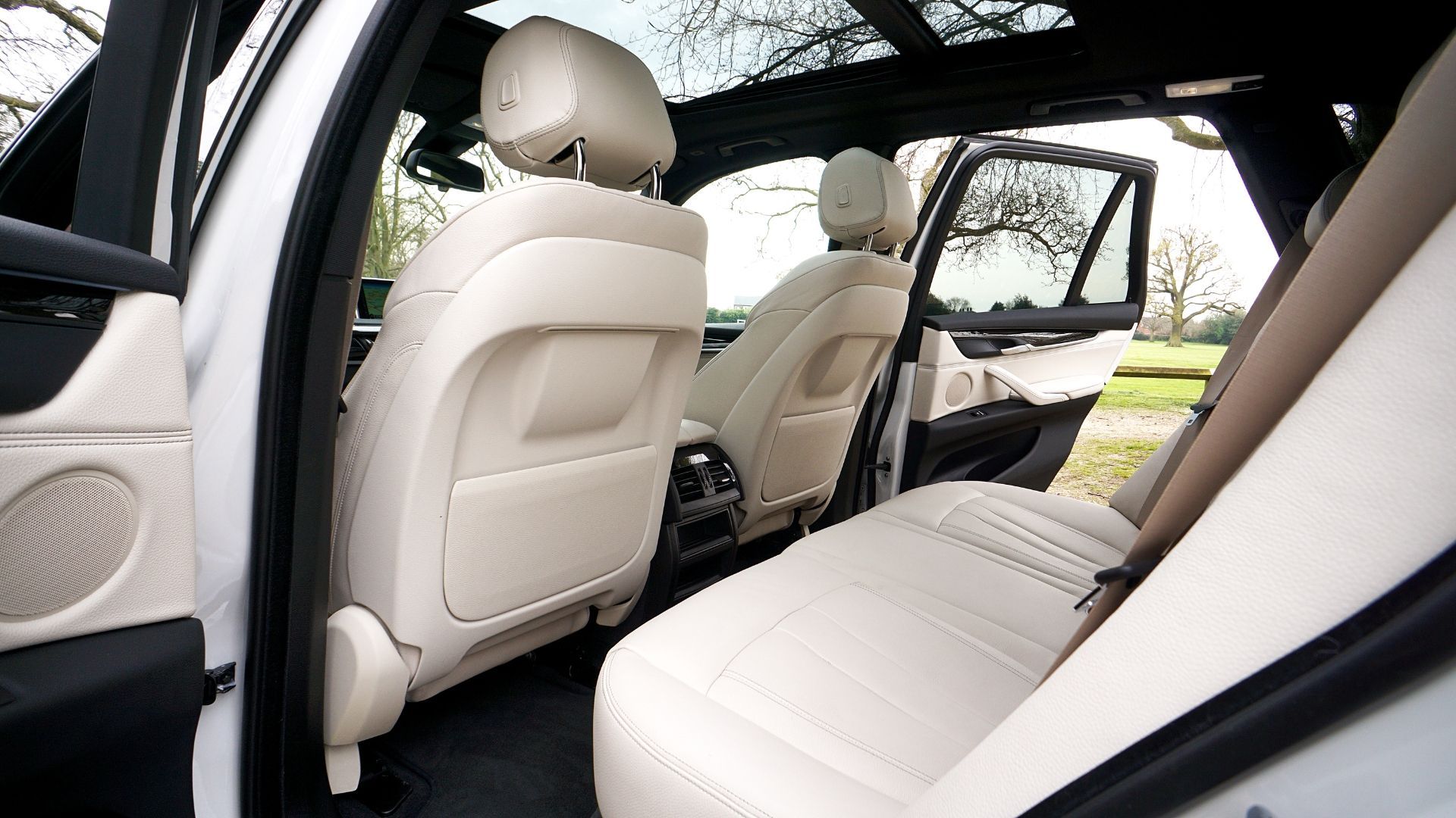 Car interior with white leather seats and open rear door, showing the back seating area.